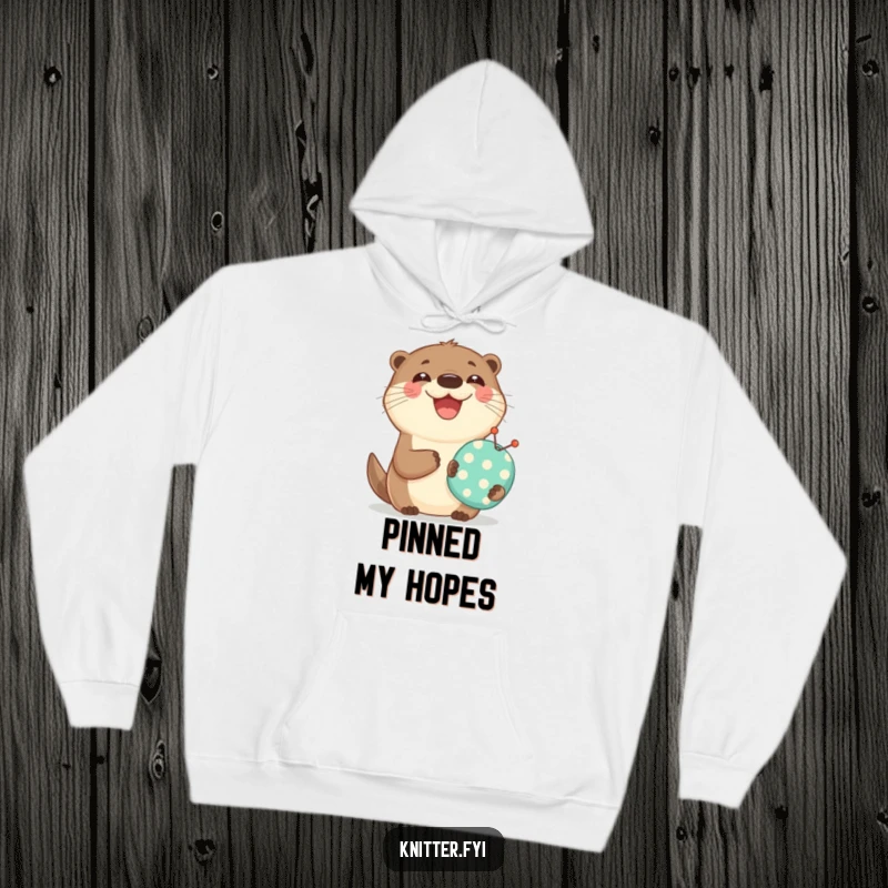 Funny hoodie depicting a happy otter holding a miniature pincushion and smiling broadly, a cozy item for crafters.